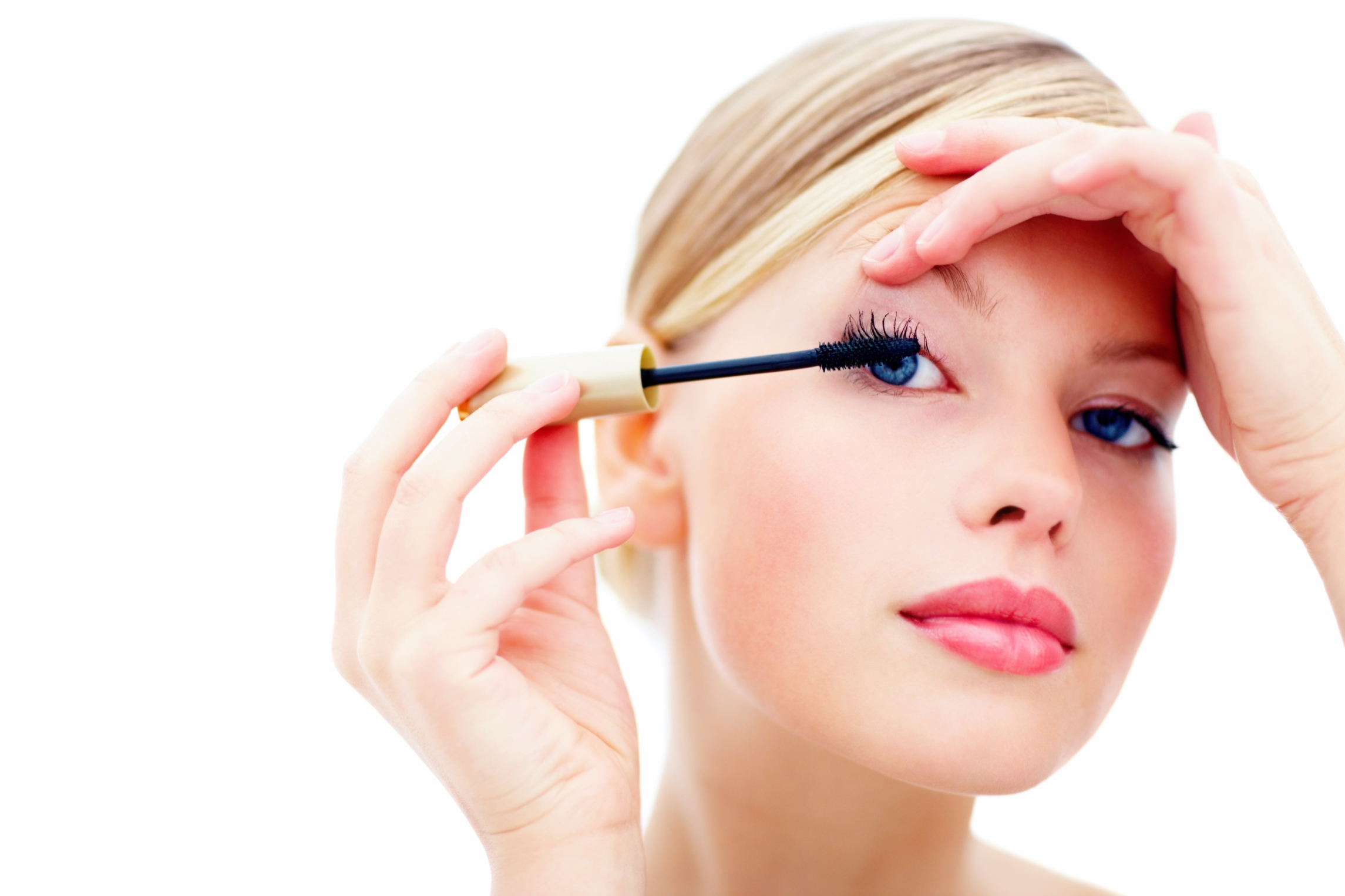 Closeup of cute female applying mascara with brush on white back